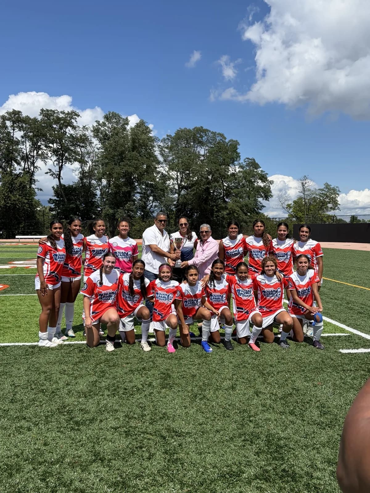 The New Jersey squad and Games officials hold the Juegos Juan Pablo Duarte trophy on the field.