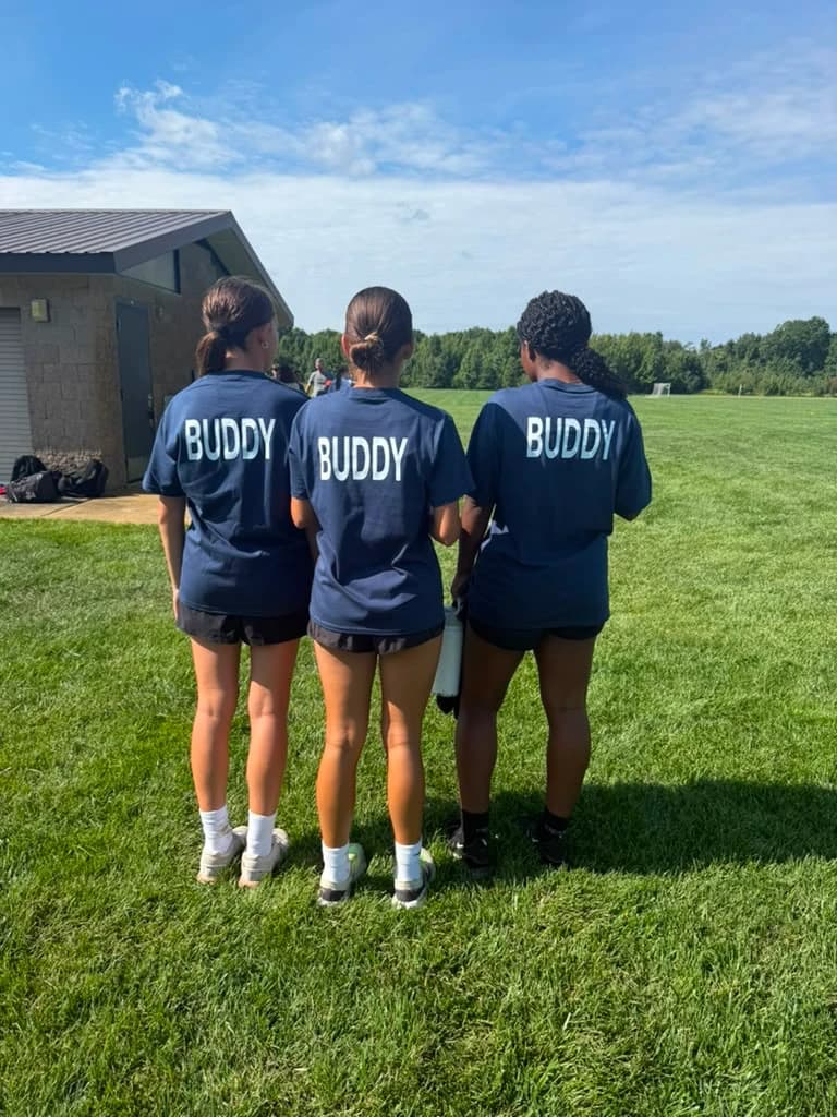 Three volunteer buddies in navy TOPSoccer shirts reading BUDDY across the back, standing together on the field.